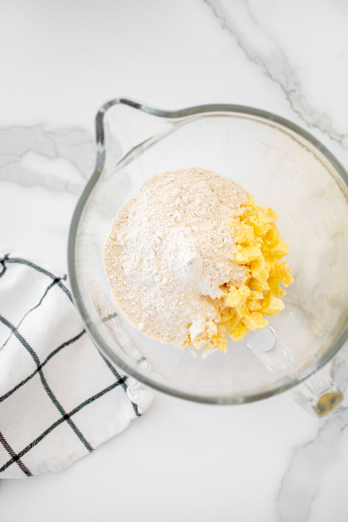 ingredients for pie dough in the bowl of a mixer on a white countertop.