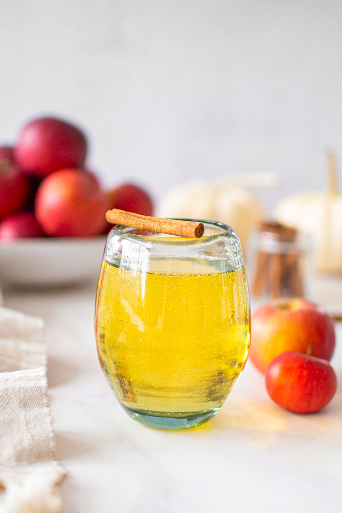 sparkling apple cider mimosa with a cinnamon stick in a stemless wine glass on a marble counntertop.