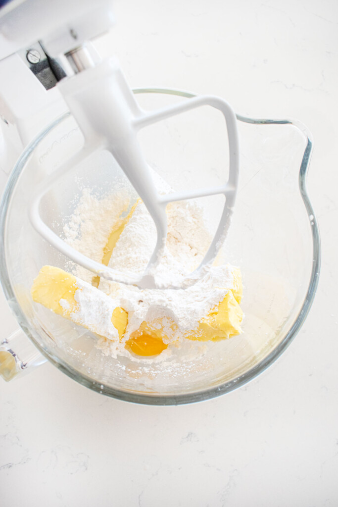 butter powdered sugar and egg yolk in a glass mixing bowl on a white marble counter.