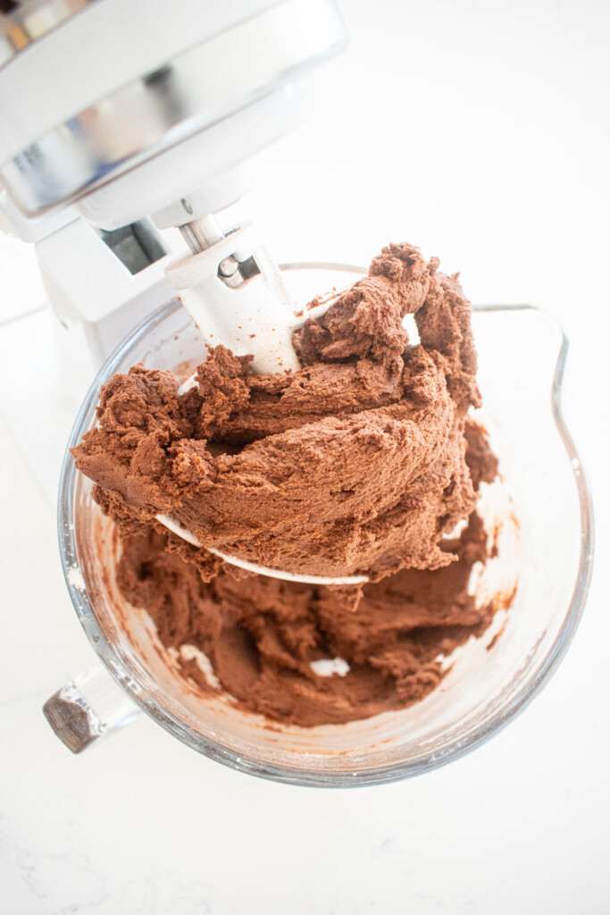 chocolate peppermint greek butter cookie dough in a glass mixing bowl on a white marble counter.