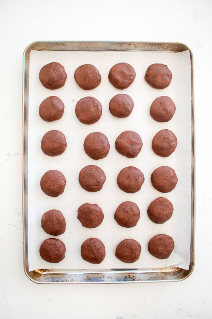 chocolate peppermint greek butter cookie dough balls on a parchment paper lined baking sheet on a marble counter.