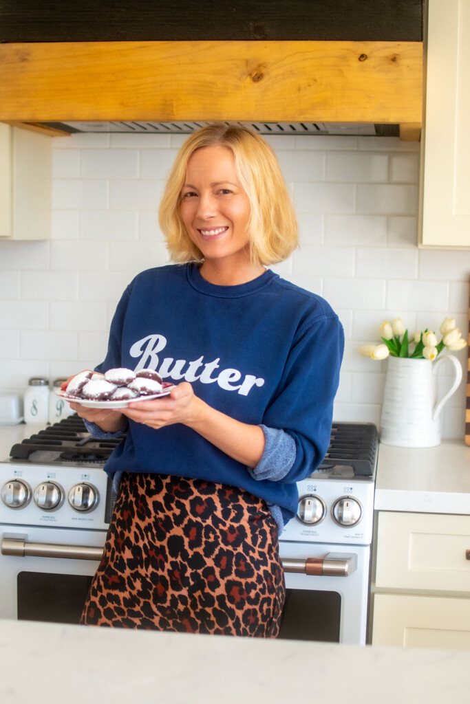 woman wearing a butter sweatshirt holding a plate of chocolate peppermint greek butter cookies in the kitchen.