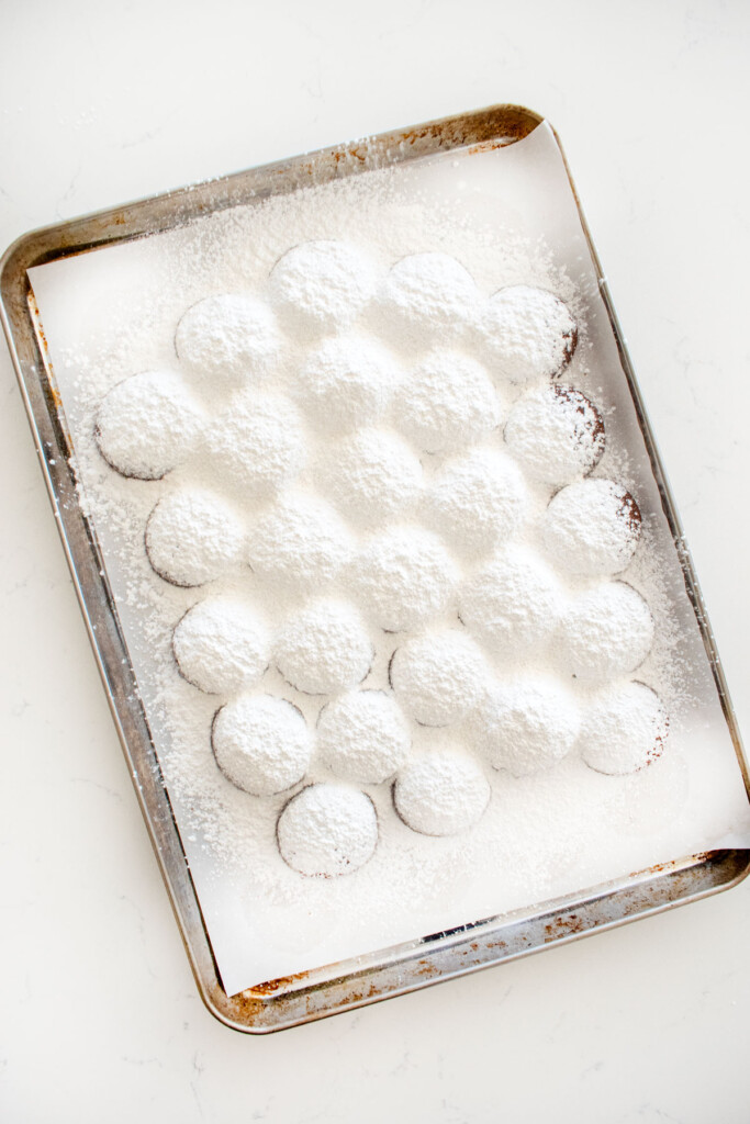 chocolate peppermint greek butter cookies with powdered sugar on them on a baking sheet on a marble counter.