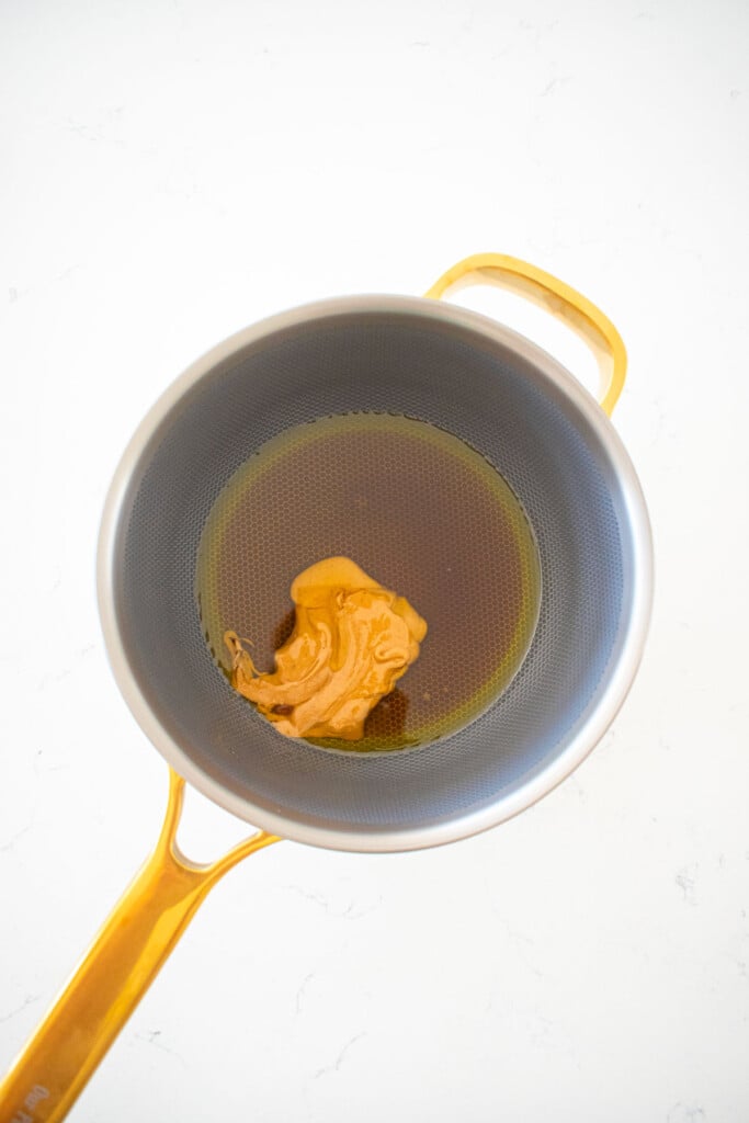 wet ingredients for easy vegan peanut brittle in a silver and gold pot on a white marble counter.
