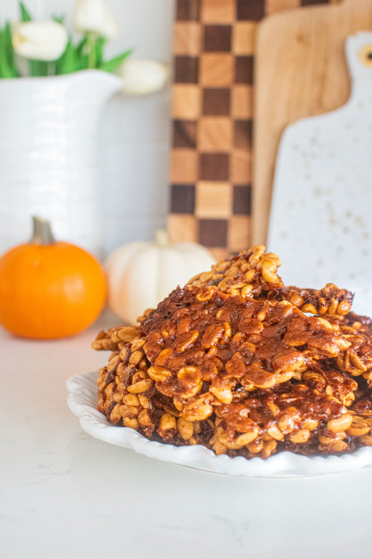 easy vegan peanut brittle on a plate on a white marble counter with pumpkins and flowers.