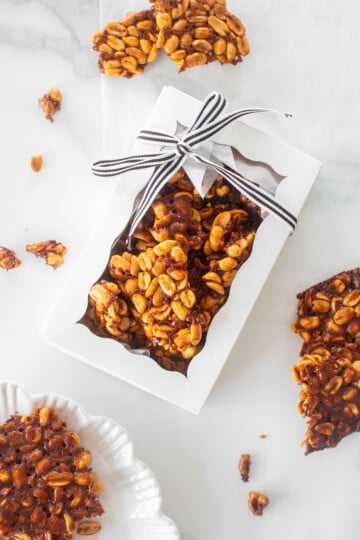 easy vegan peanut brittle in a white gift box tied with a black and white stripe ribbon on a marble counter.