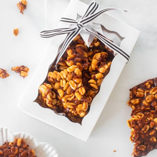 easy vegan peanut brittle in a white gift box tied with a black and white stripe ribbon on a marble counter.