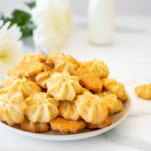 plate of eggless spritz cookies on a marble counter with fresh flowers.
