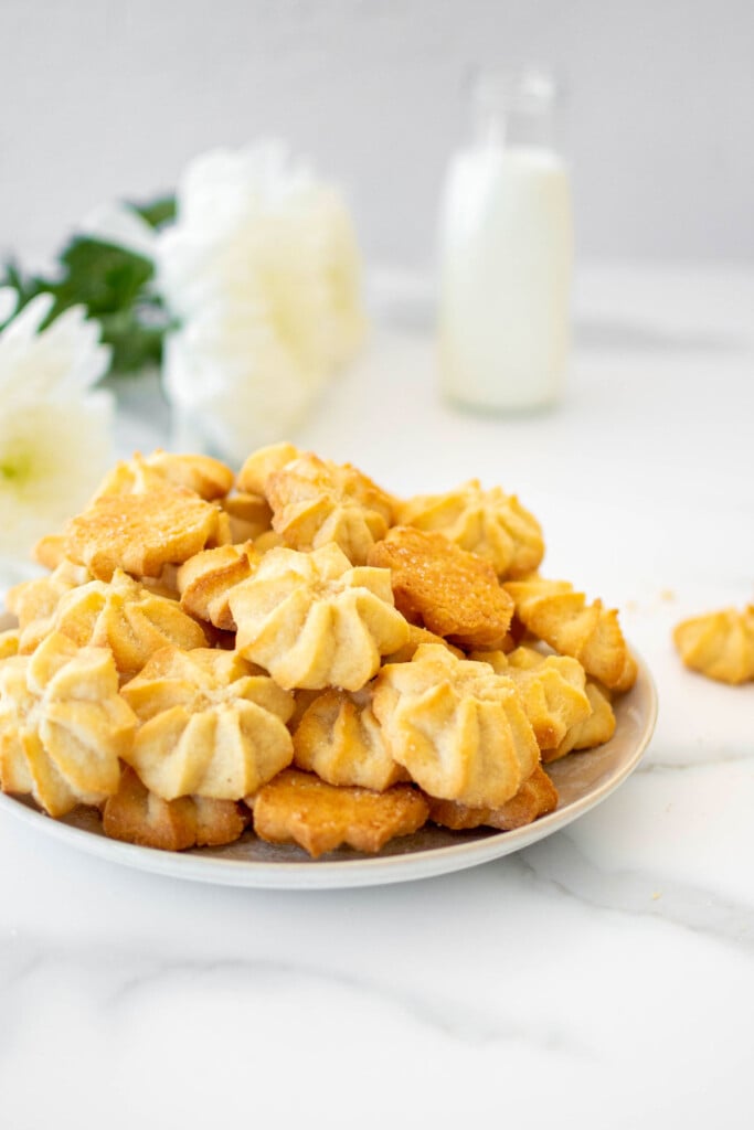 plate of eggless spritz cookies on a marble counter with fresh flowers.