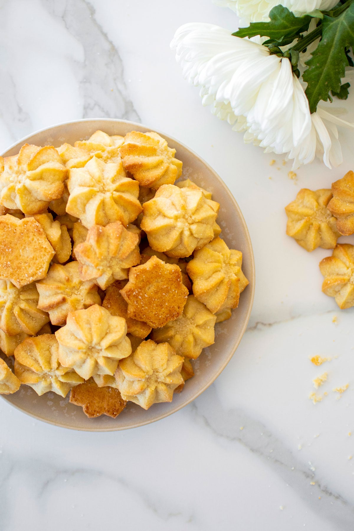 plate of eggless spritz cookies on a marble counter with fresh flowers.