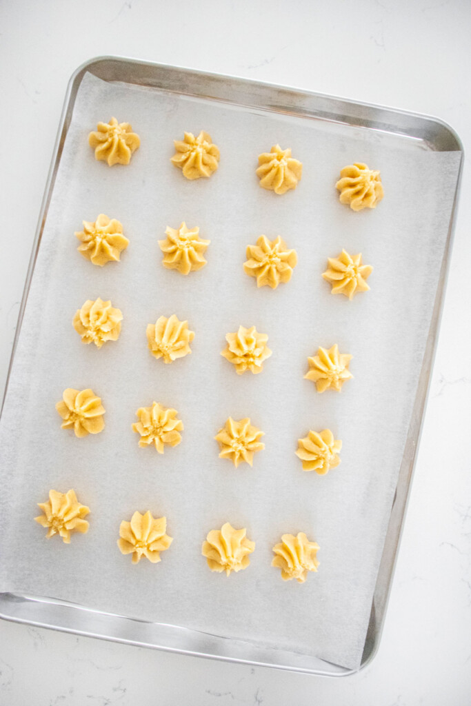 piped eggless spritz cookie dough on a baking sheet on a marble counter.