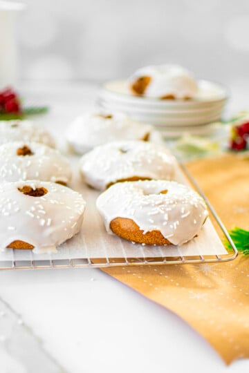 frosted gingerbread donuts on a cooling rack on a white marble countertop.