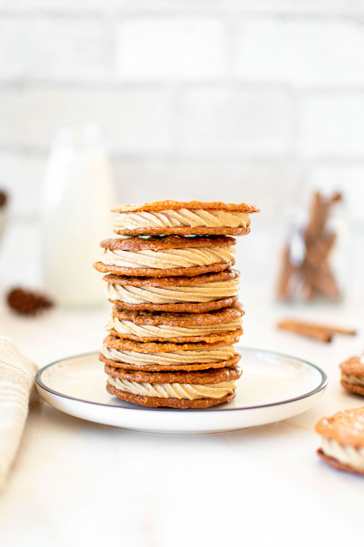 stack of gingerbread florentine sandwich cookies on a plate with a glass milk bottle on a white marble counter.