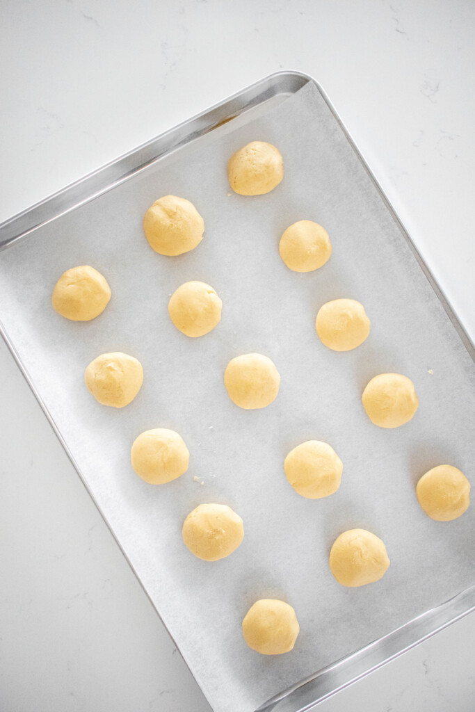 raw vanilla shortbread cookie dough balls on a baking sheet on a white marble countertop.