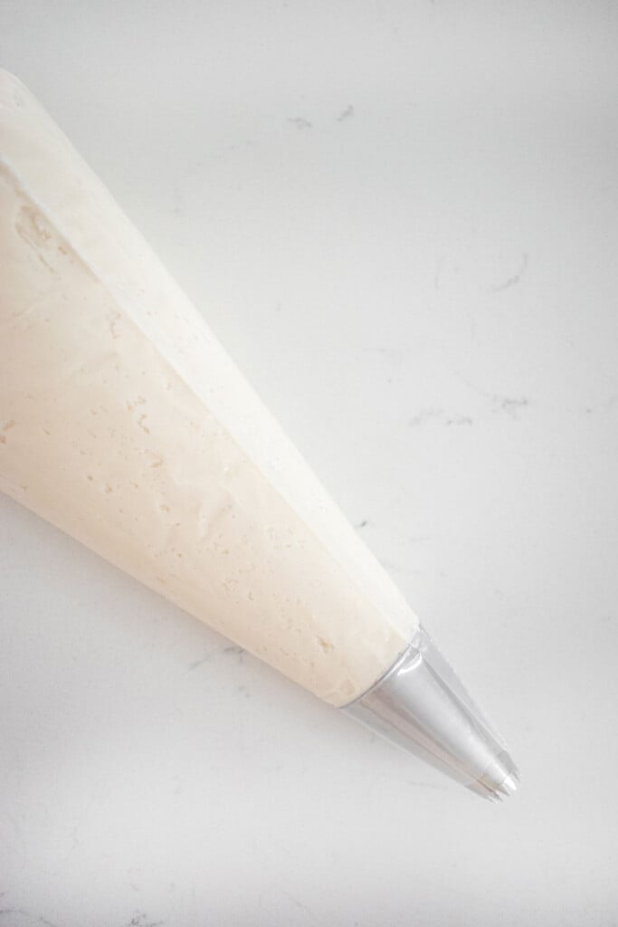 vanilla frosting in a piping bag with decorating tip on a white marble countertop.