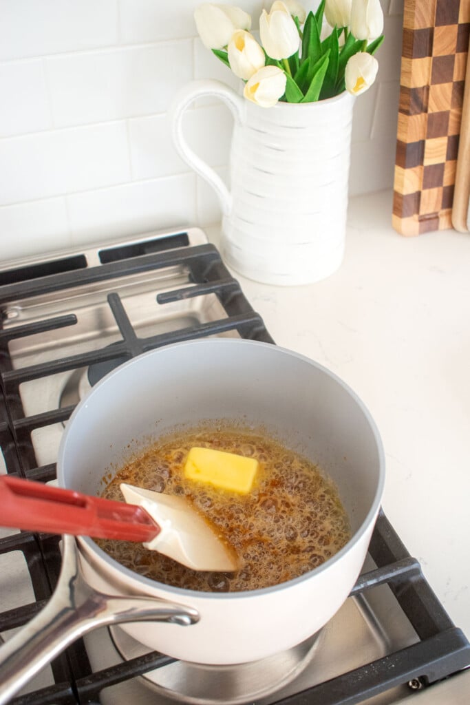butter being added to melted sugar in a pot on a stovetop.
