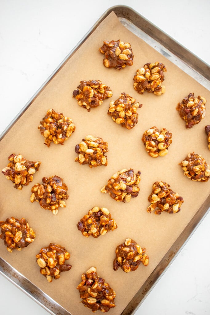 peanut and caramel clusters on a parchment paper lined baking sheet.