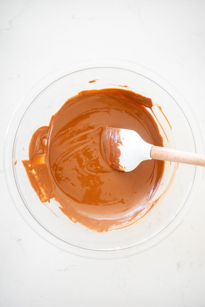 melted milk chocolate in a glass bowl on a white marble counter.