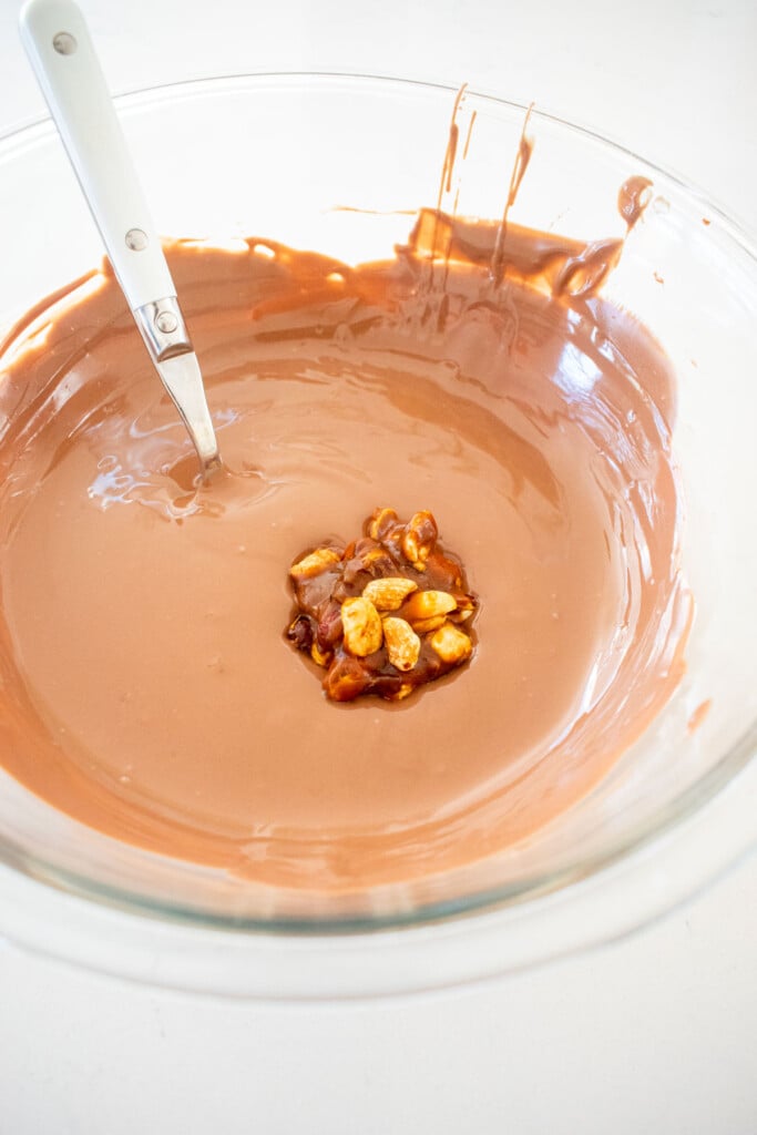 melted milk chocolate in a glass bowl with a caramel peanut cluster dropped into it.