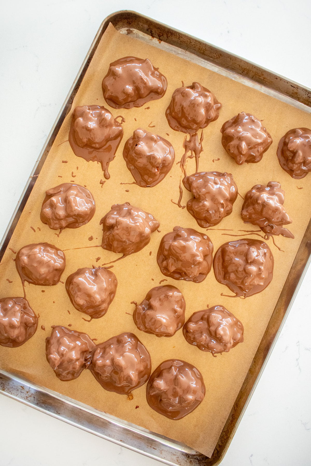 peanut turtle candies coated in chocolate on a parchment paper lined baking sheet on a white marble counter.