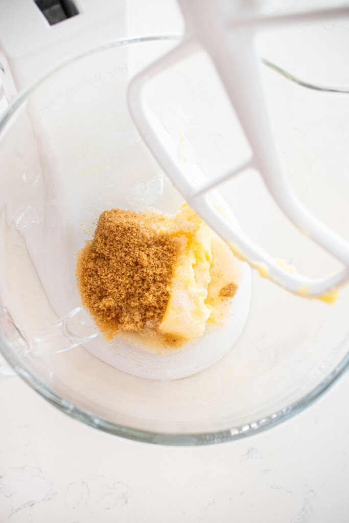 butter sugar and light brown sugar in a glass mixing bowl on a white marble counter.