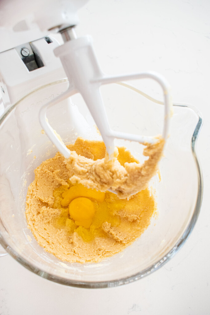 creamed butter and sugar in a glass mixing bowl with eggs on a white marble counter.