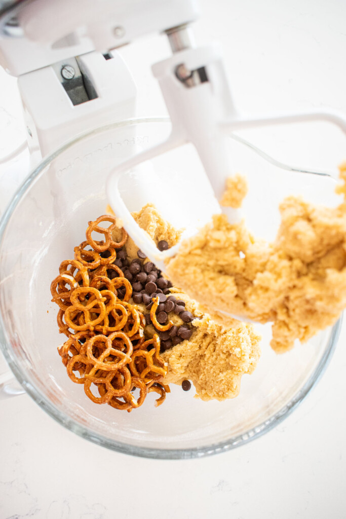 peppermint cookie dough in a glass mixing bowl with chocolate chips and mini pretzel twists.