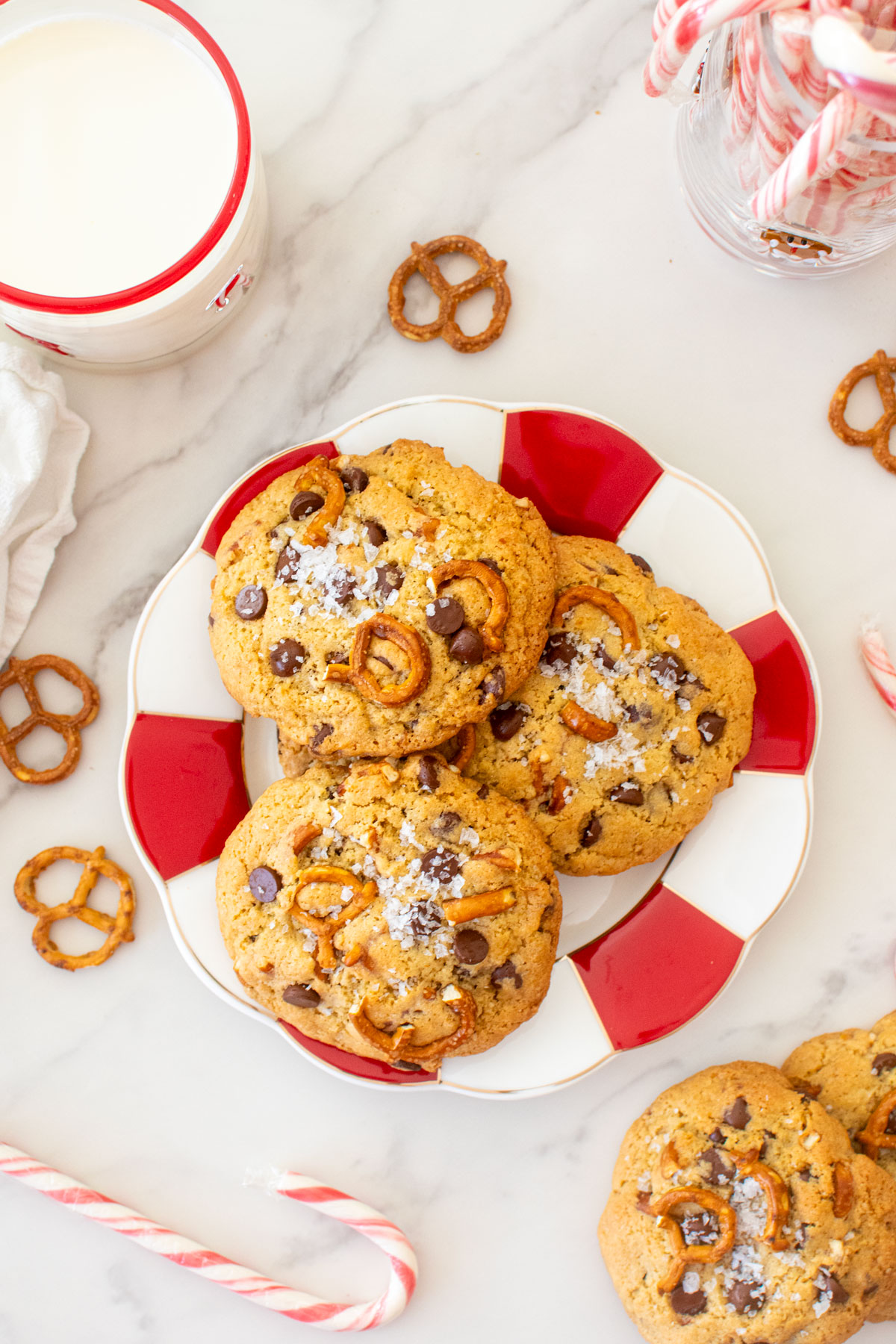 plate of peppermint pretzel chocolate chip cookies on a marble counter with a glass of milk.