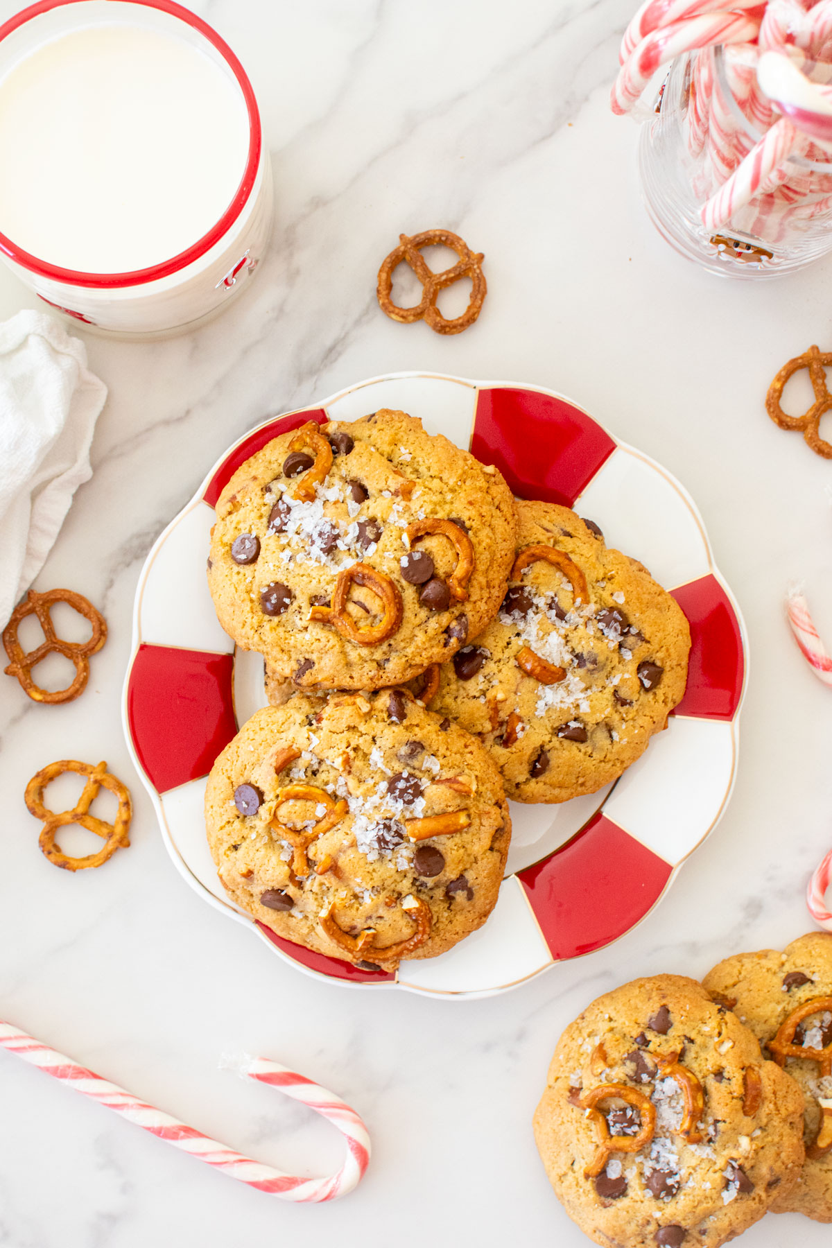 plate of peppermint pretzel chocolate chip cookies on a marble counter with a glass of milk.