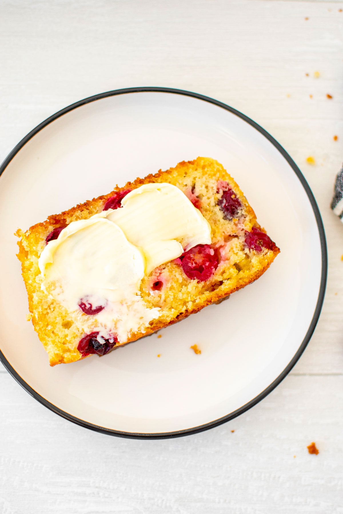 slice of cranberry orange apple bread on a white plate with a smear of butter.