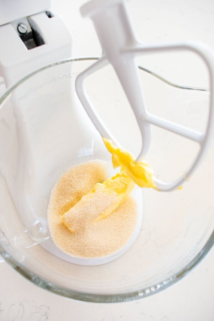 butter and cane sugar in a glass mixing bowl on a white marble counter.