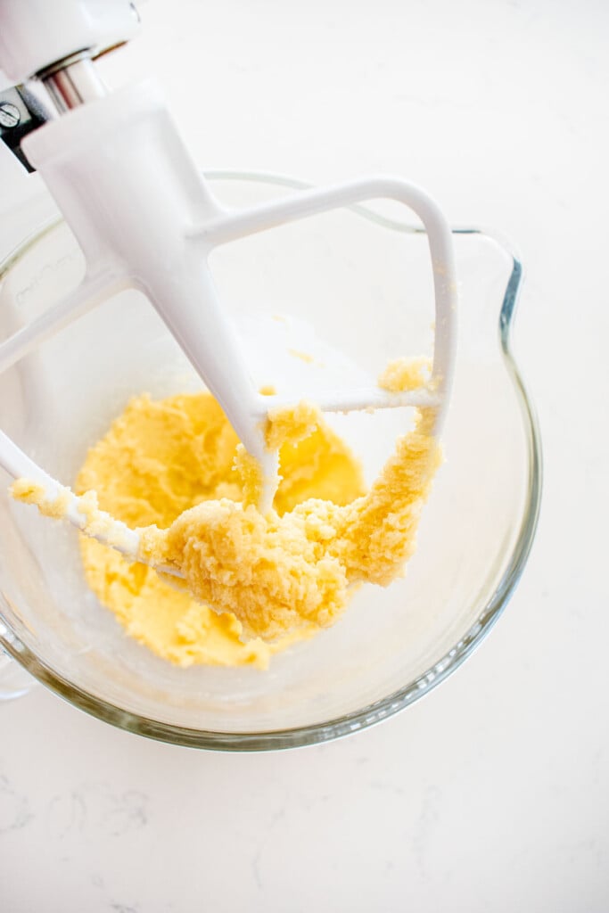 creamed butter and sugar in a glass mixing bowl on a white marble counter.