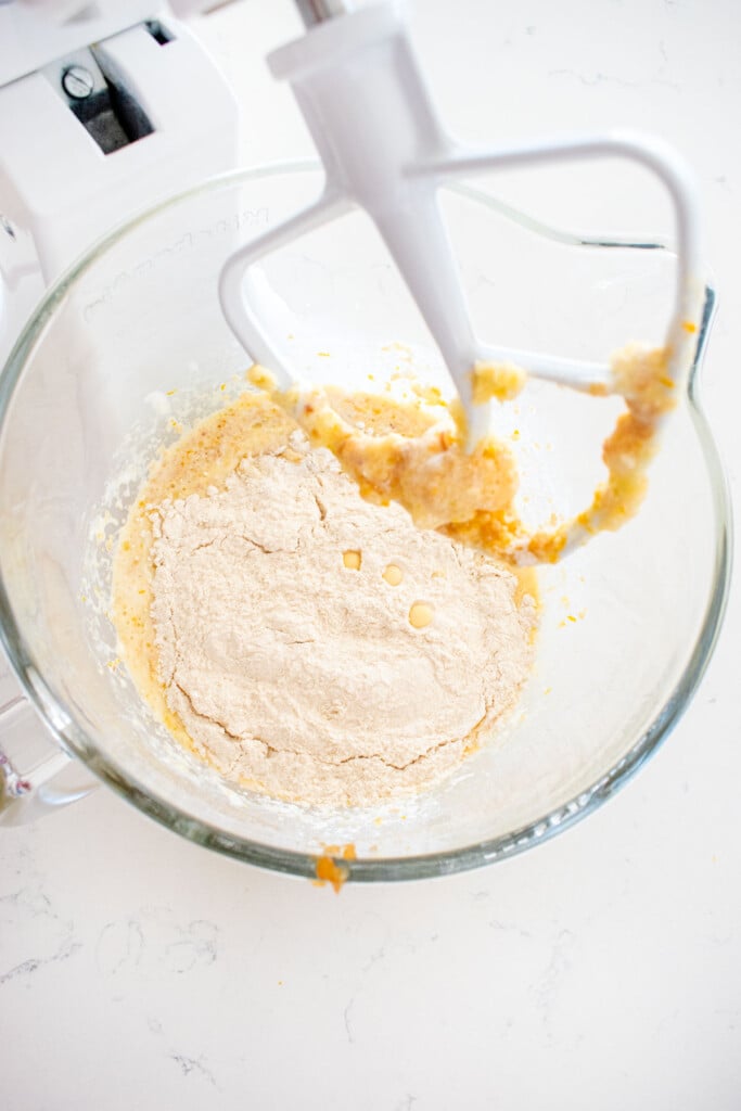 ingredients for cranberry orange apple bread in a glass mixing bowl on a white marble counter.