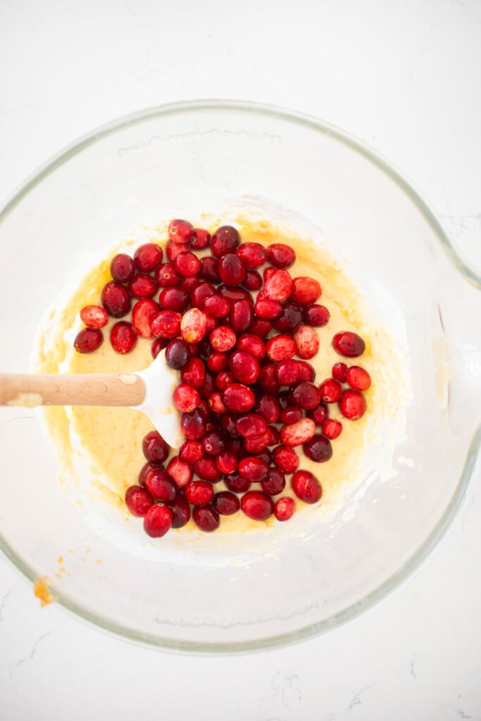 fresh cranberries in batter in a glass mixing bowl on a white marble counter.