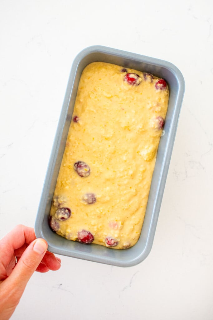 cranberry orange apple bread batter in a loaf pan on a white marble counter.