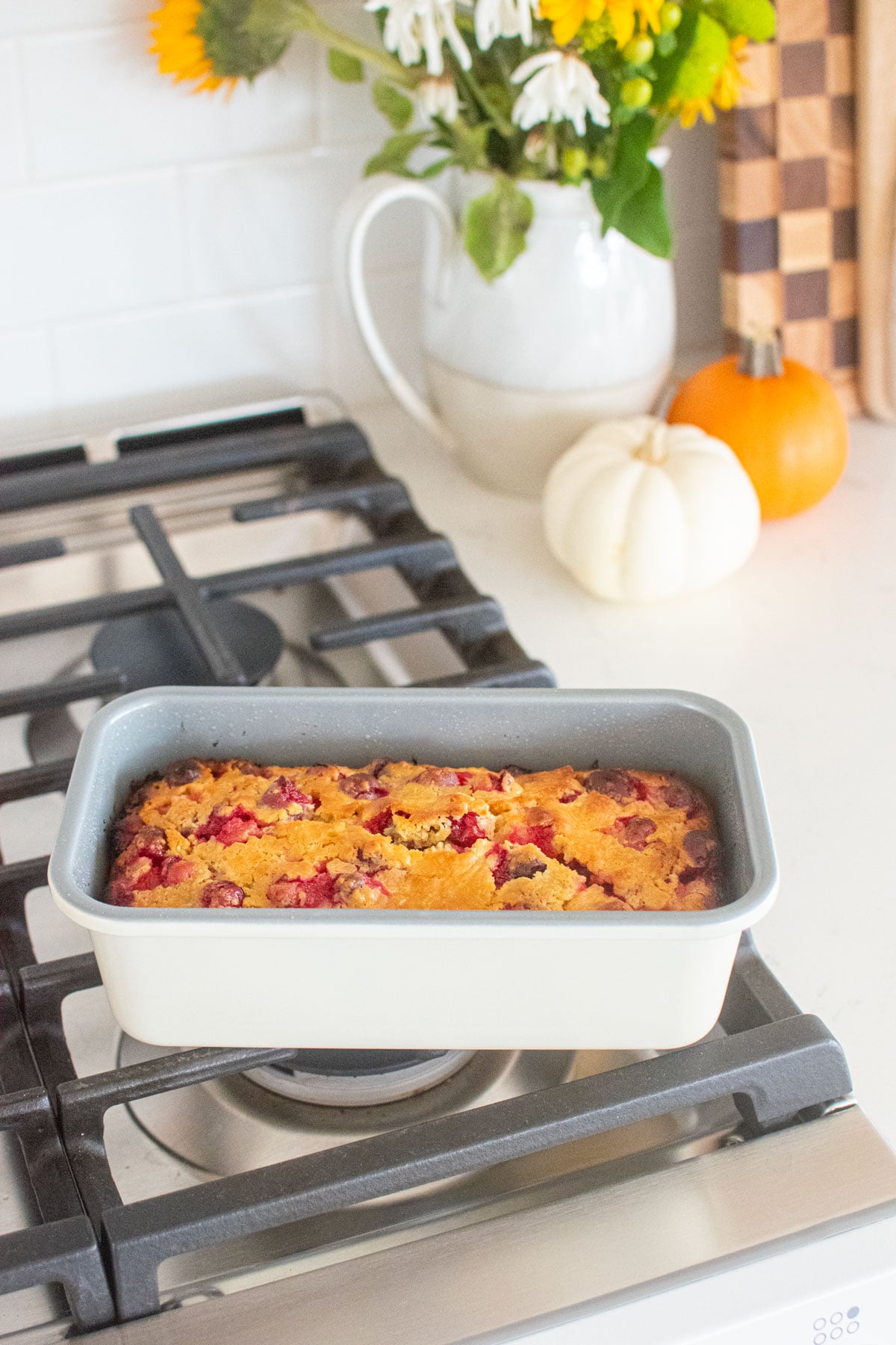 cranberry orange apple bread in a loaf pan cooling on top of the oven.