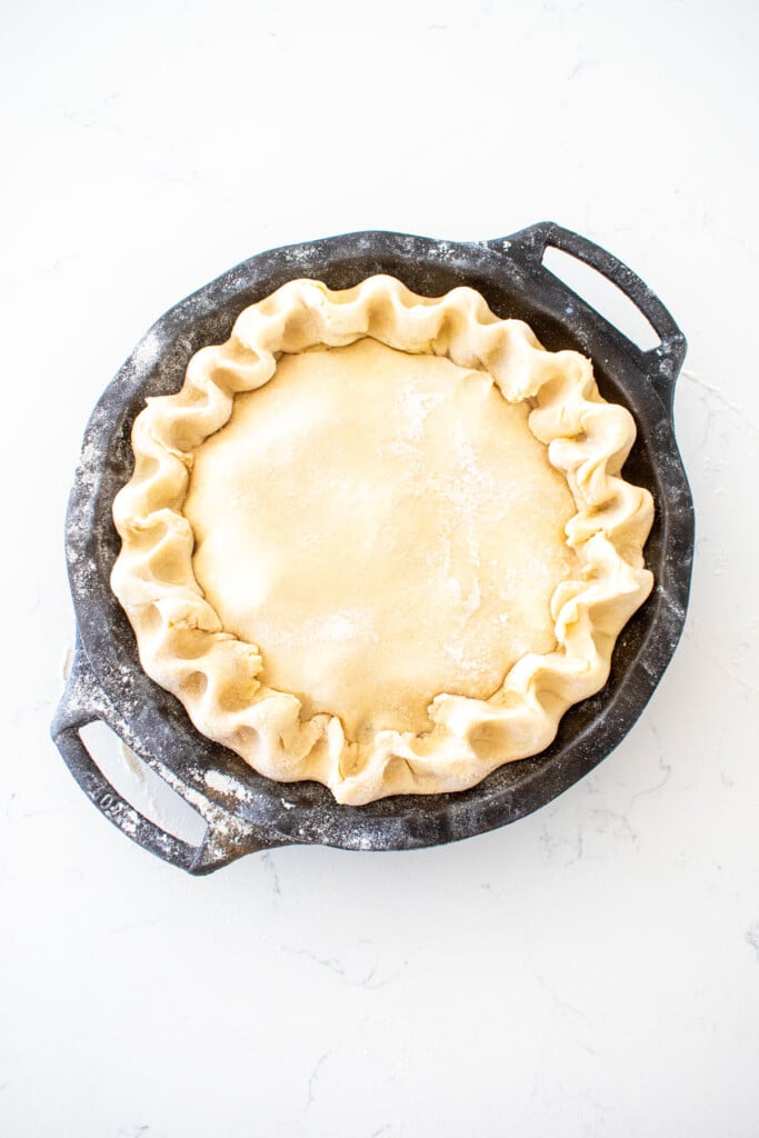 cherry pie with fluted crust in a black cast iron pie pan on a white marble counter.