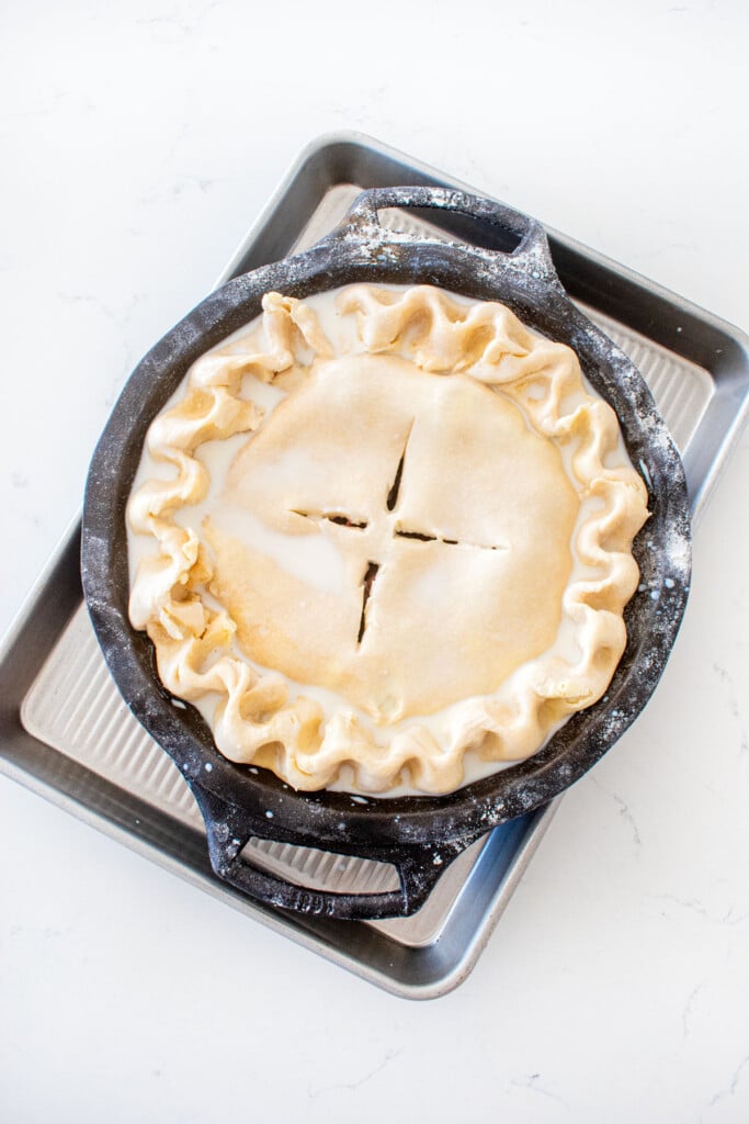 cherry pie with milk brushed on top, fluted, and vented on a quarter sheet pan on a white marble counter.