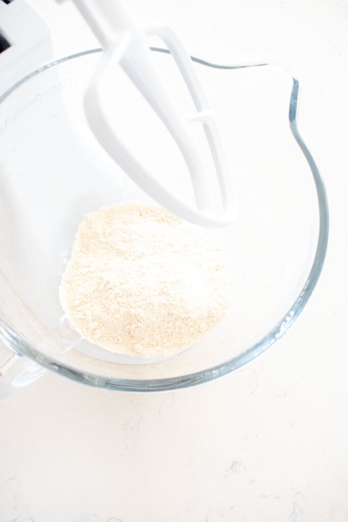 flour in a glass mixing bowl on a white marble counter.