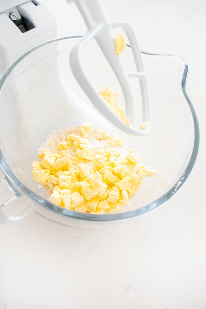flour and butter in a glass mixing bowl on a white marble counter.