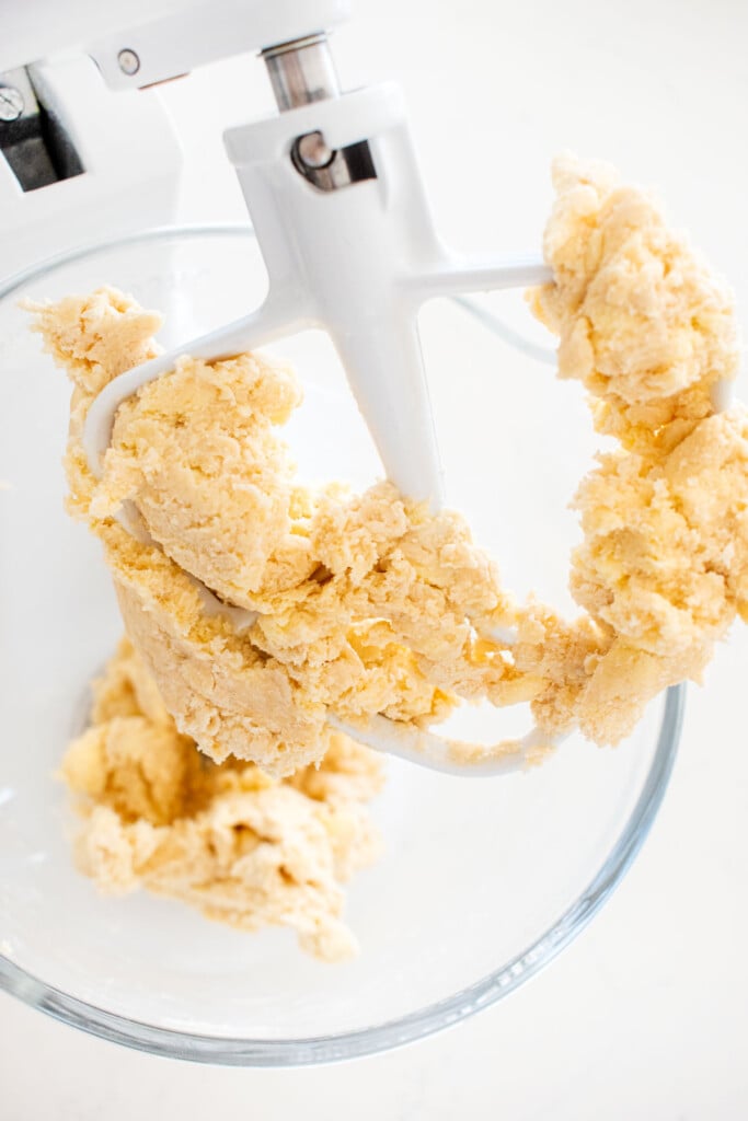 pie crust in a glass stand mixing bowl on a white marble counter.