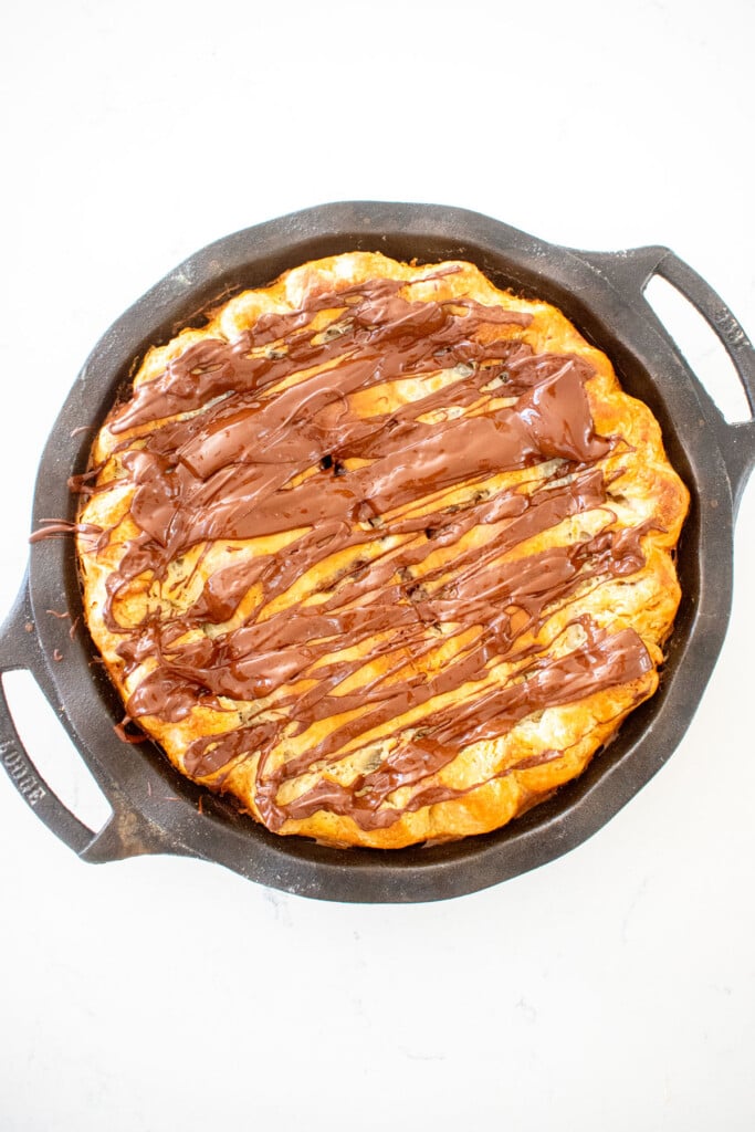 cherry chocolate chip pie with melted dark chocolate drizzled on top in a cast iron pie pan on a white marble counter.