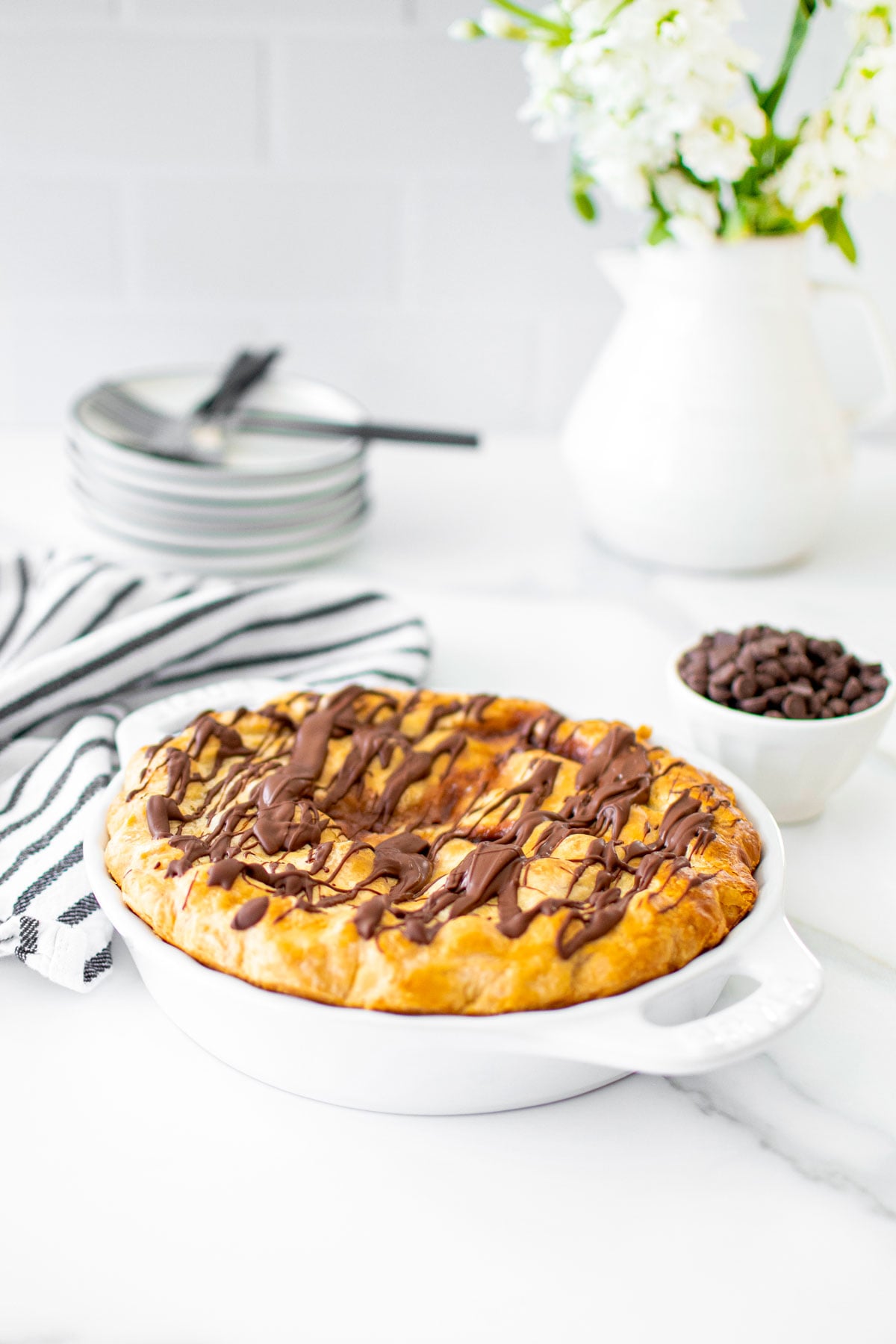 cherry chocolate chip pie in a white pie dish on a white marble table with fresh flowers.