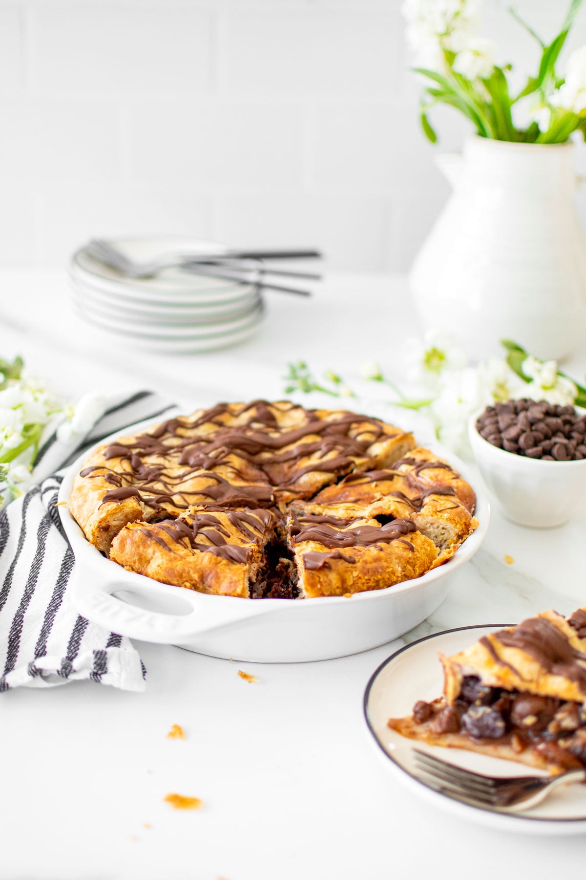 cherry chocolate chip pie in a white pie dish on a white marble table with fresh flowers.