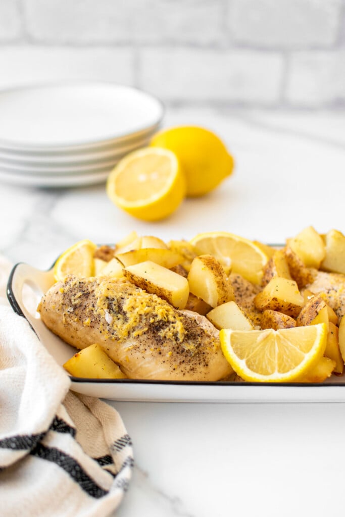 greek lemon chicken and potatoes in a white serving dish on a marble countertop.