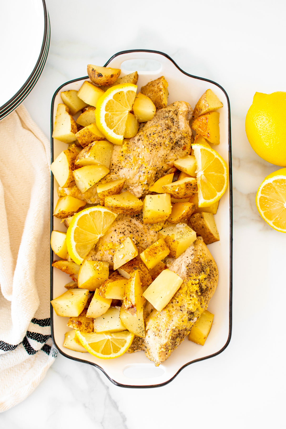 greek lemon chicken and potatoes in a white serving dish on a marble countertop.