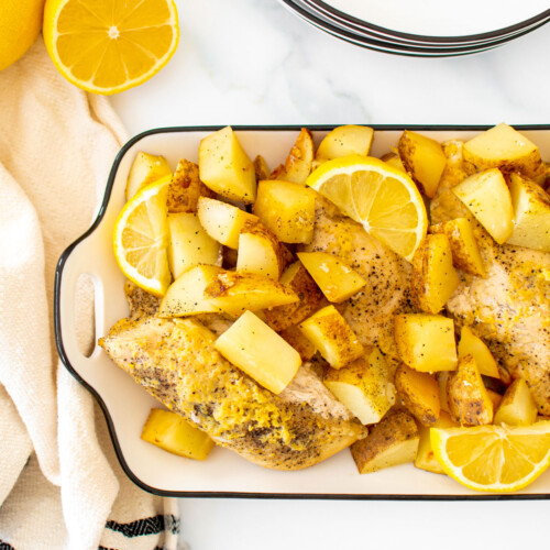 greek lemon chicken and potatoes in a white serving dish on a marble countertop.