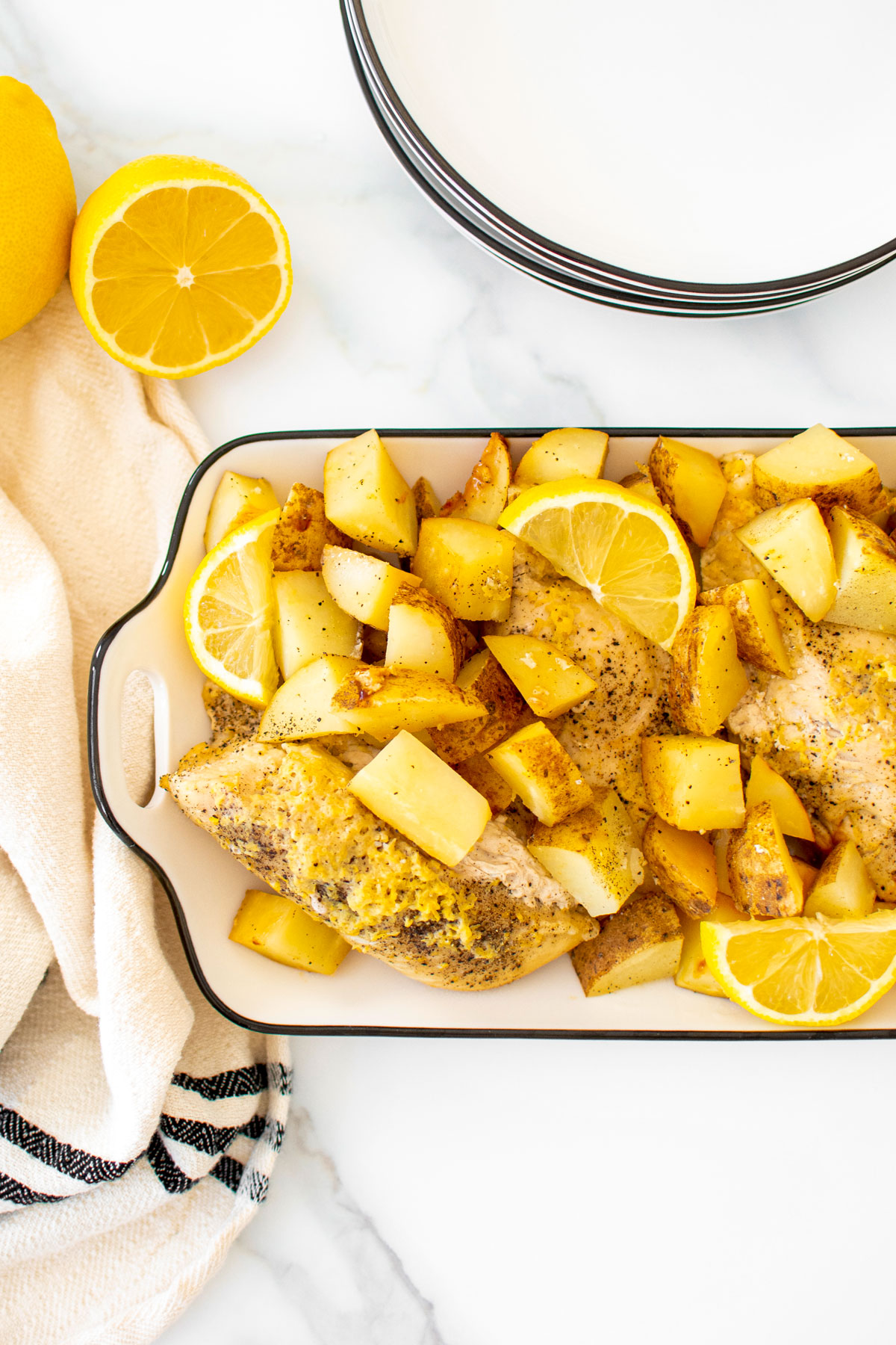 greek lemon chicken and potatoes in a white serving dish on a marble countertop.