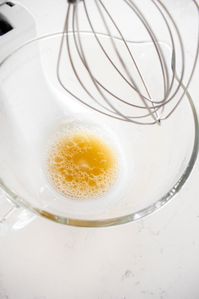 gelatin blooming in a glass stand mixing bowl with a whisk on a marble counter.
