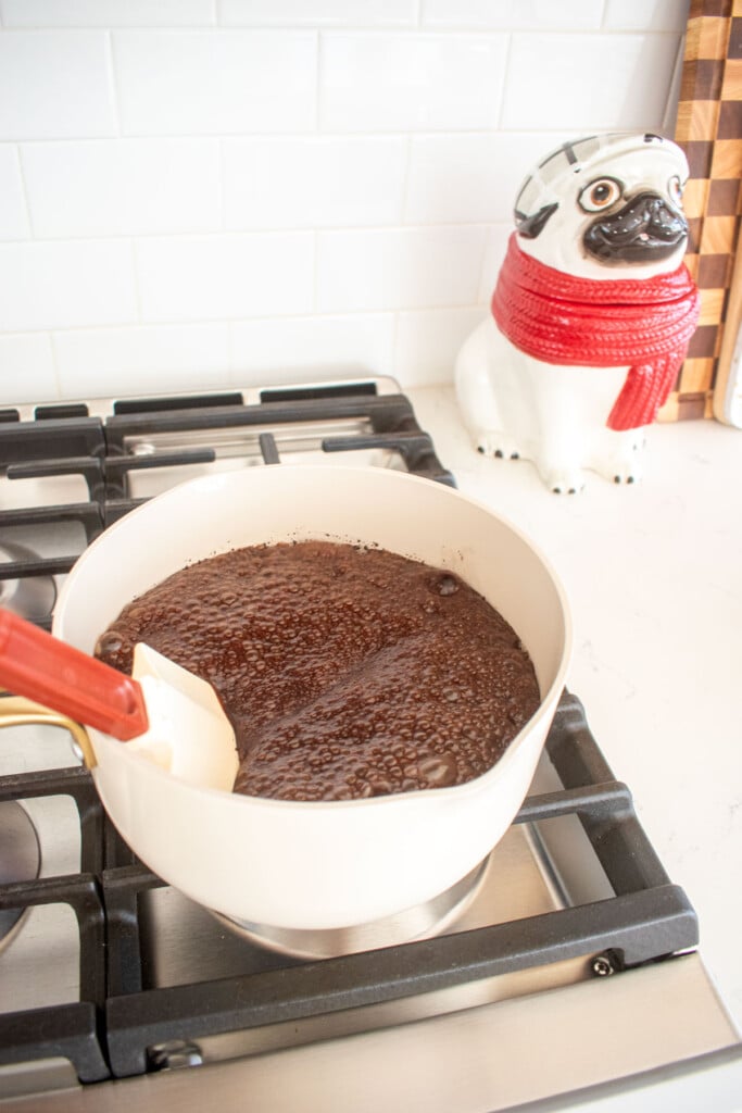 ingredients for homemade chocolate marshmallows being stirred with a spatula bubbling and rising up in a small pot on the stovetop.
